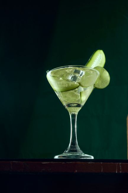 A tall glass of a pink mocktail with ice, a lime wheel, and a mint sprig on a bar counter next to fresh citrus.