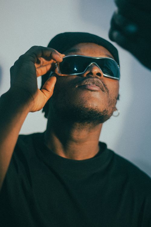 Free A stylish man wearing sunglasses poses confidently under dramatic lighting. Stock Photo