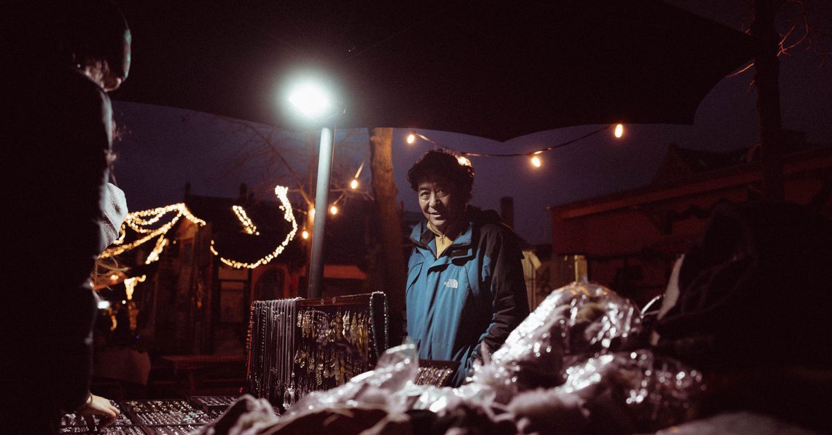 A vendor at a night market interacting with customers under twinkling string lights.