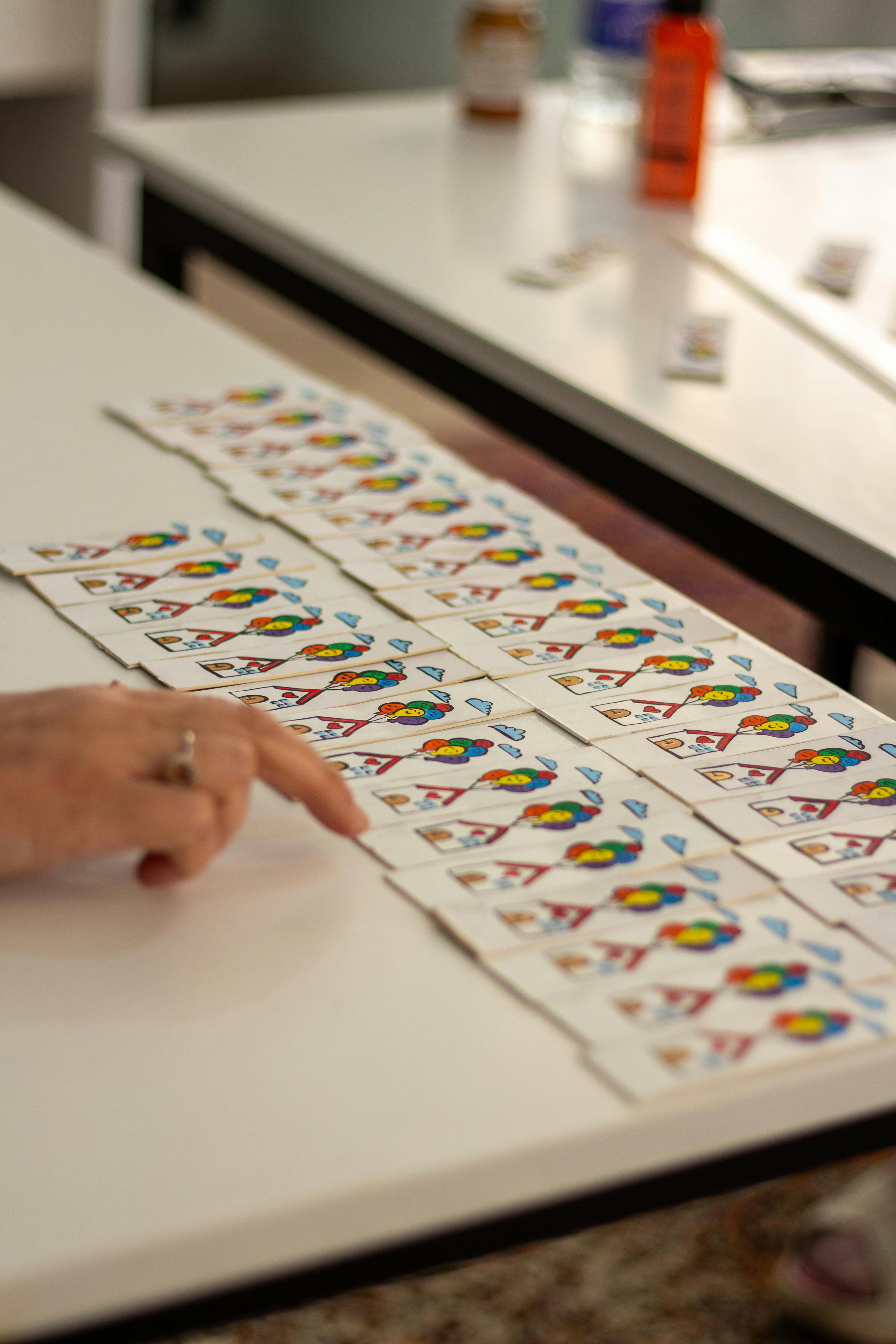 Person's hand pointing at rows of playing cards on a table indoors.