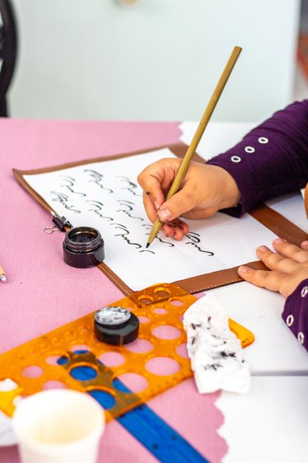 A person practicing calligraphy with ink and pen on paper, close-up view.