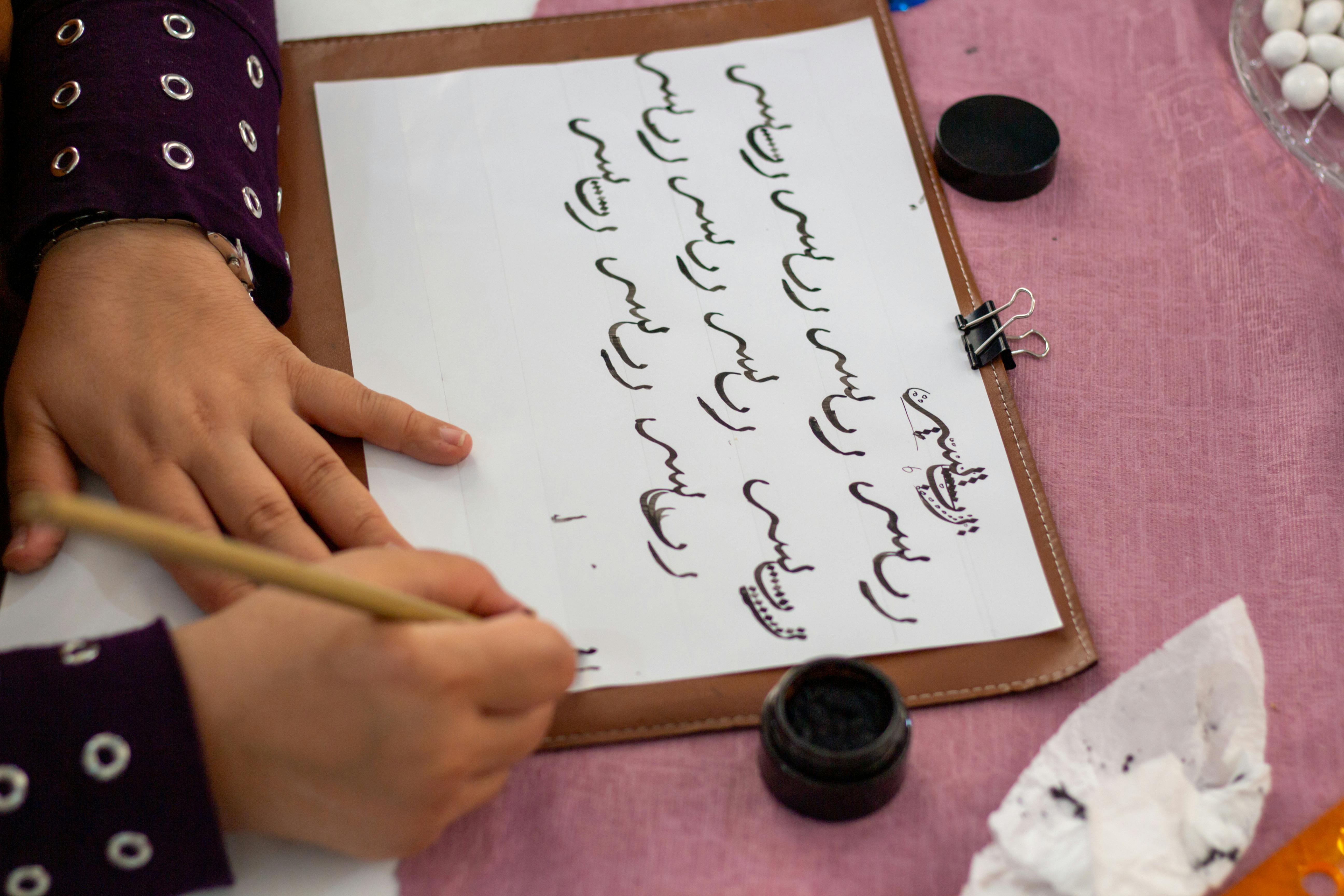 Hands practicing traditional calligraphy on a clipboard with ink and brush.