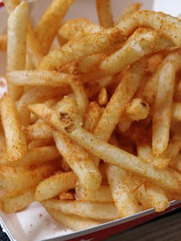Tasty and crispy seasoned French fries in a paper box, perfect for a snack.
