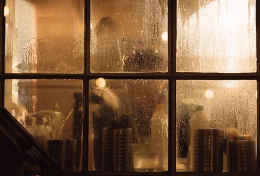 Moody view through a fogged window into a cozy interior with warm lighting.