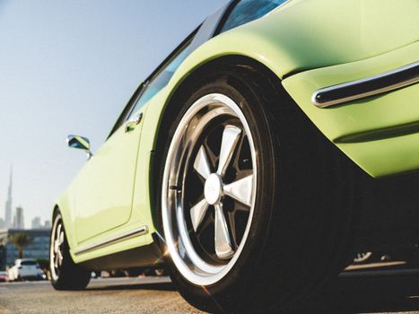 Low-angle view of a classic green sports car with city skyline in daylight.