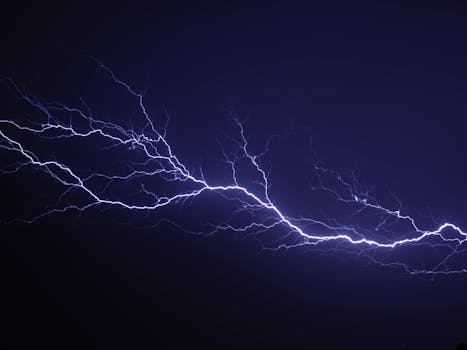 A dramatic capture of a bright blue lightning bolt against a dark night sky.