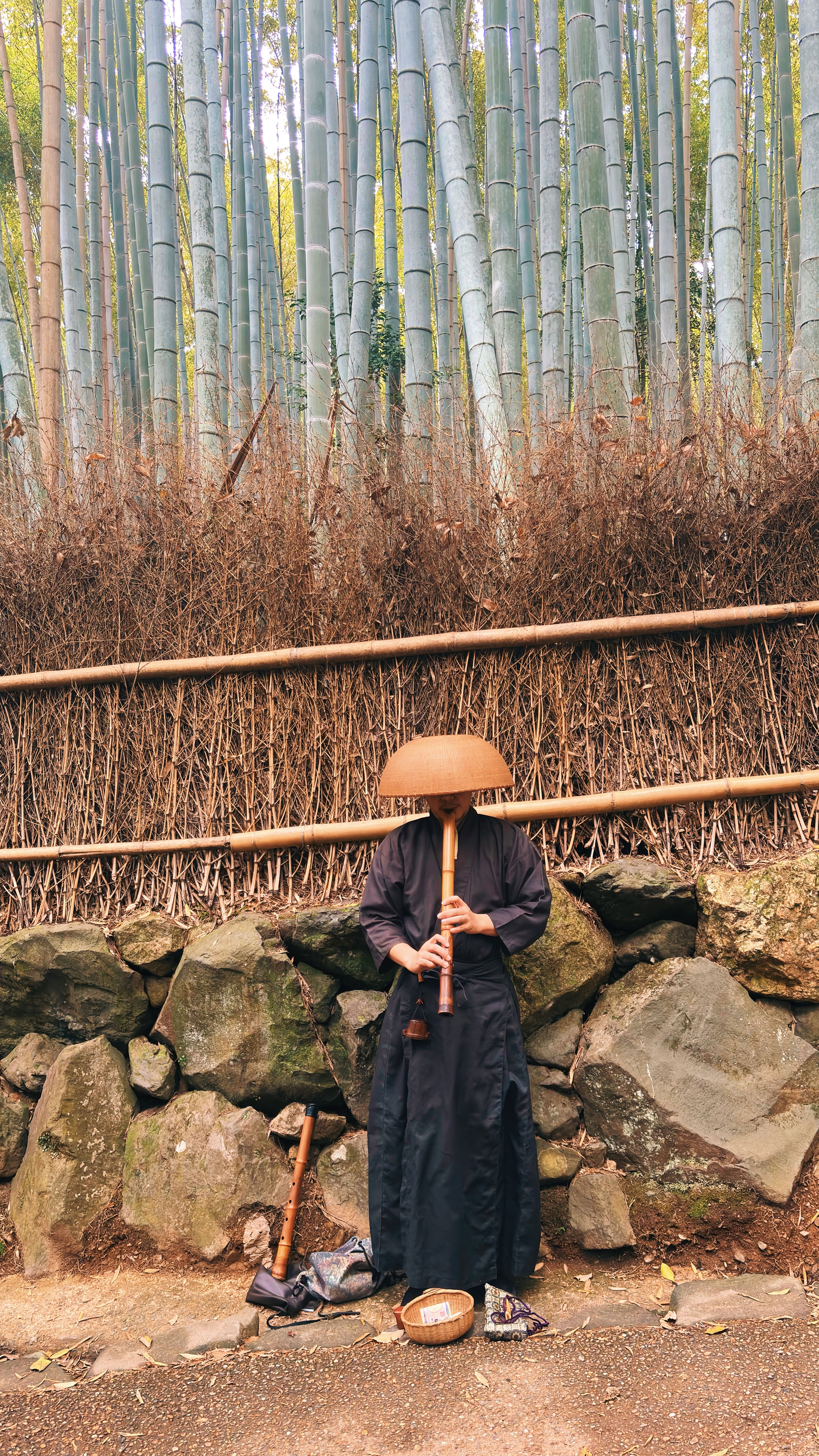 A man in traditional attire playing flute in a bamboo forest.
