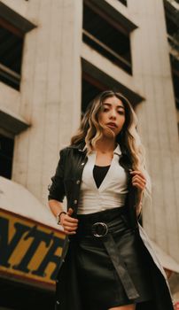 Stylish woman in a cityscape wearing a leather jacket, looking confident.