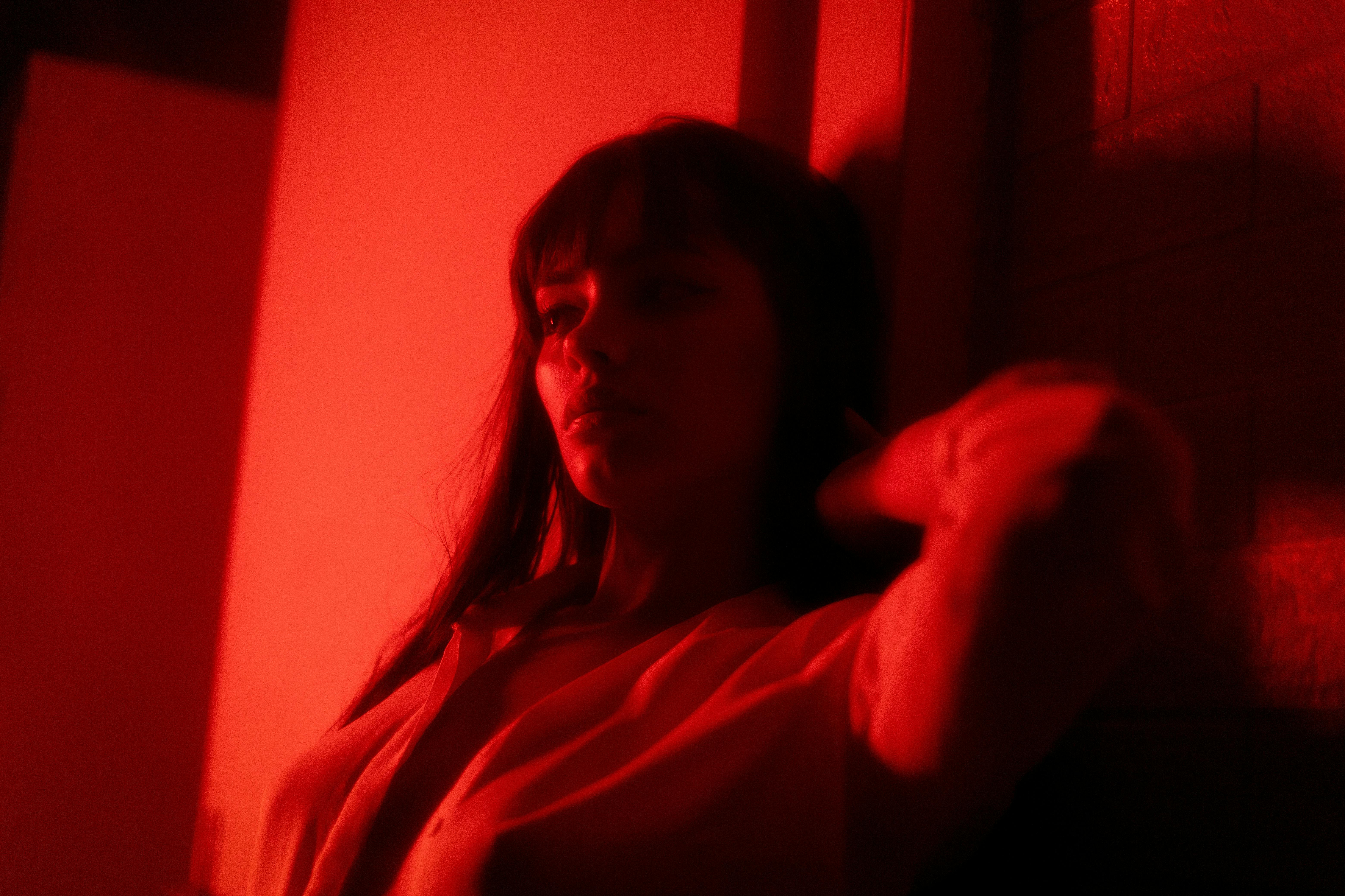 Gratis Retrato artístico de una mujer bajo una tenue iluminación roja, creando una atmósfera misteriosa y melancólica. Foto de stock