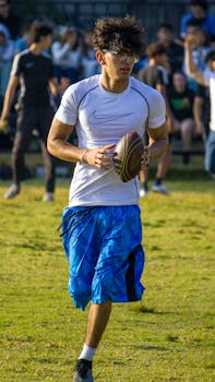 A young athlete holding a football while running on a grassy field outdoors.