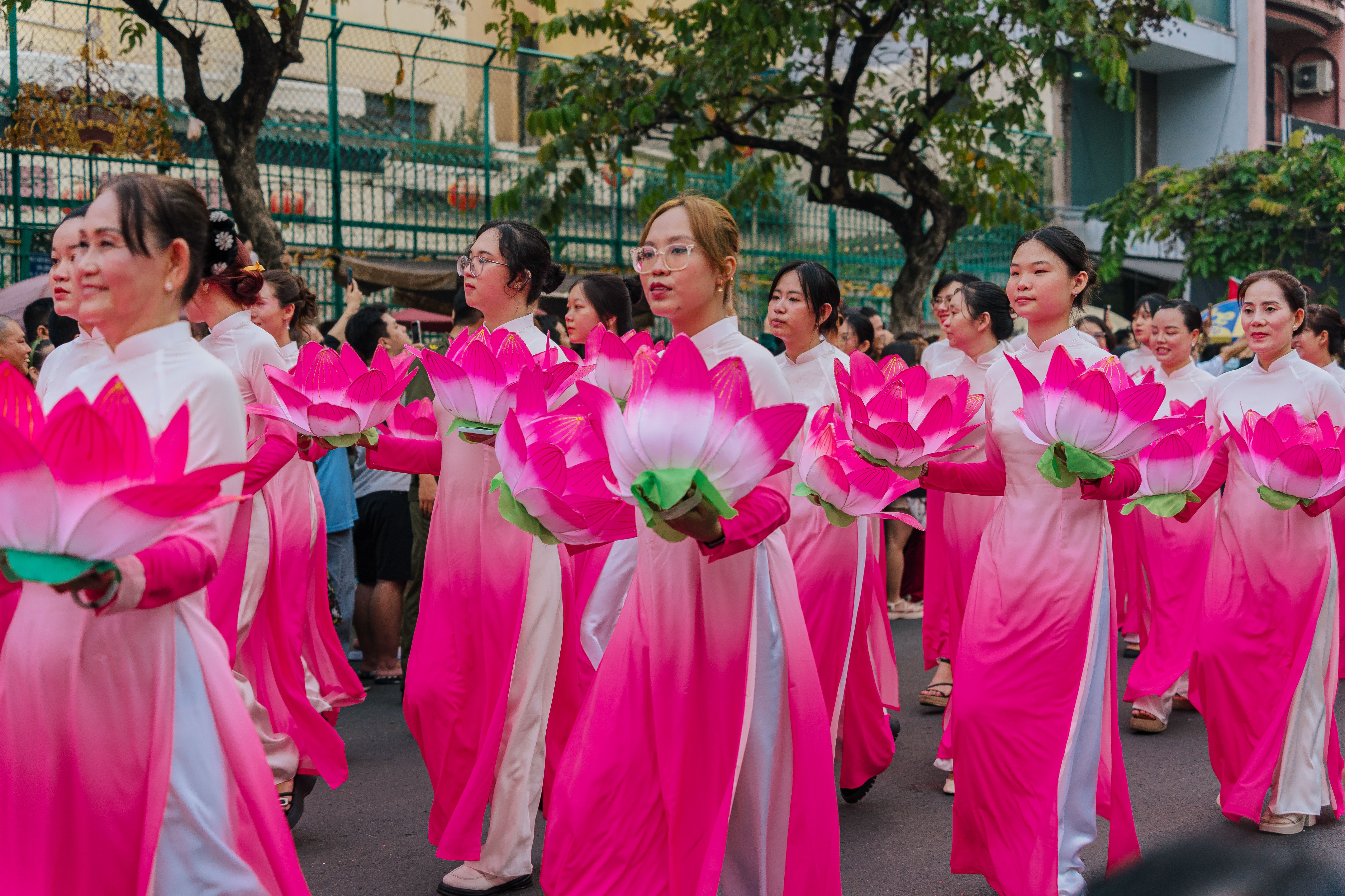 Women in pink áo dài holding lotus flowers in a vibrant parade.