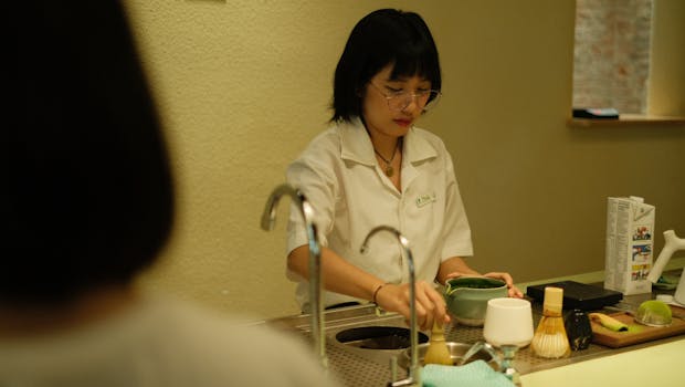 Young adult preparing traditional tea indoors at a counter, focused and serene.