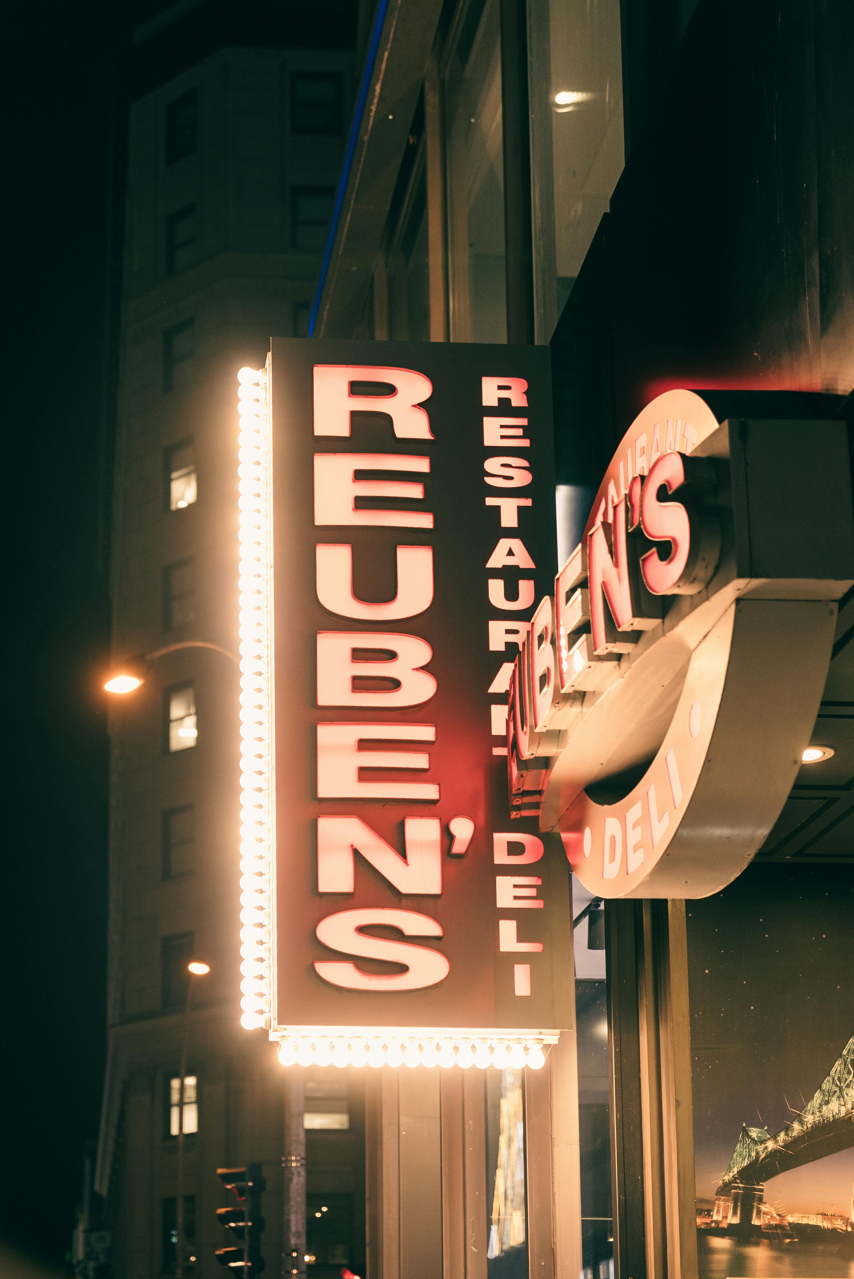 Ücretsiz Kentsel bir gece fonunda Reuben's Deli'nin parlayan neon tabelası. Stok Fotoğraflar
