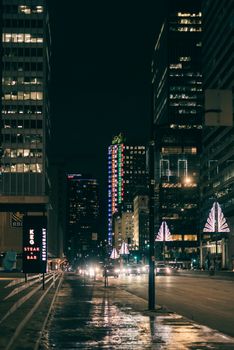 Vibrant city street at night with lit skyscrapers and festive lights.