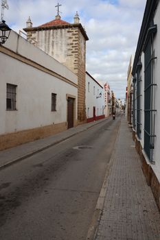 Charming narrow street in Puerto Real, Spain, showcasing historic architecture under cloudy skies.