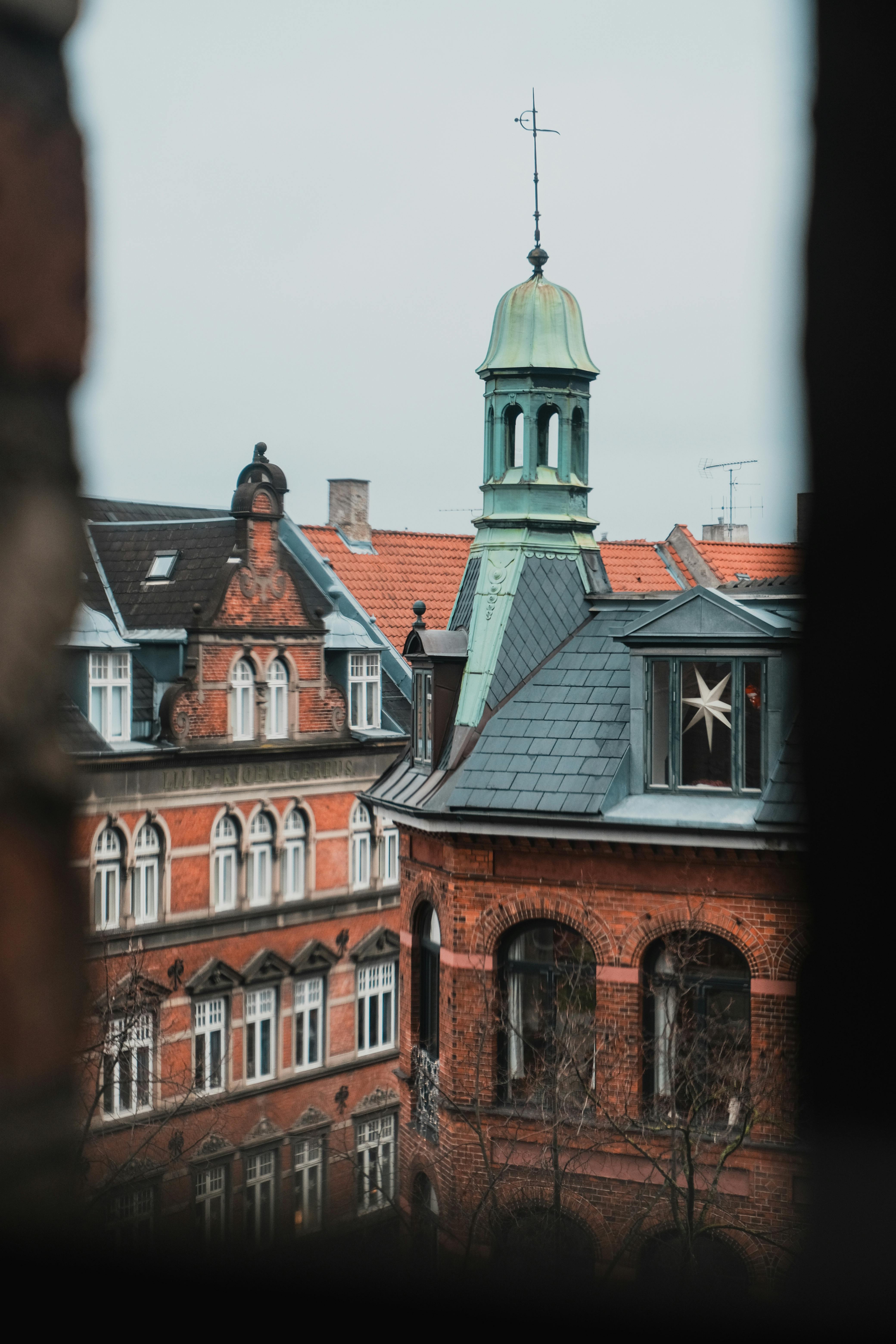 View of historic European rooftops and towers seen through a window frame in Copenhagen.