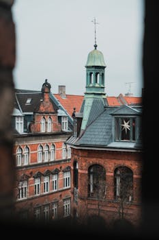 View of historic European rooftops and towers seen through a window frame in Copenhagen.
