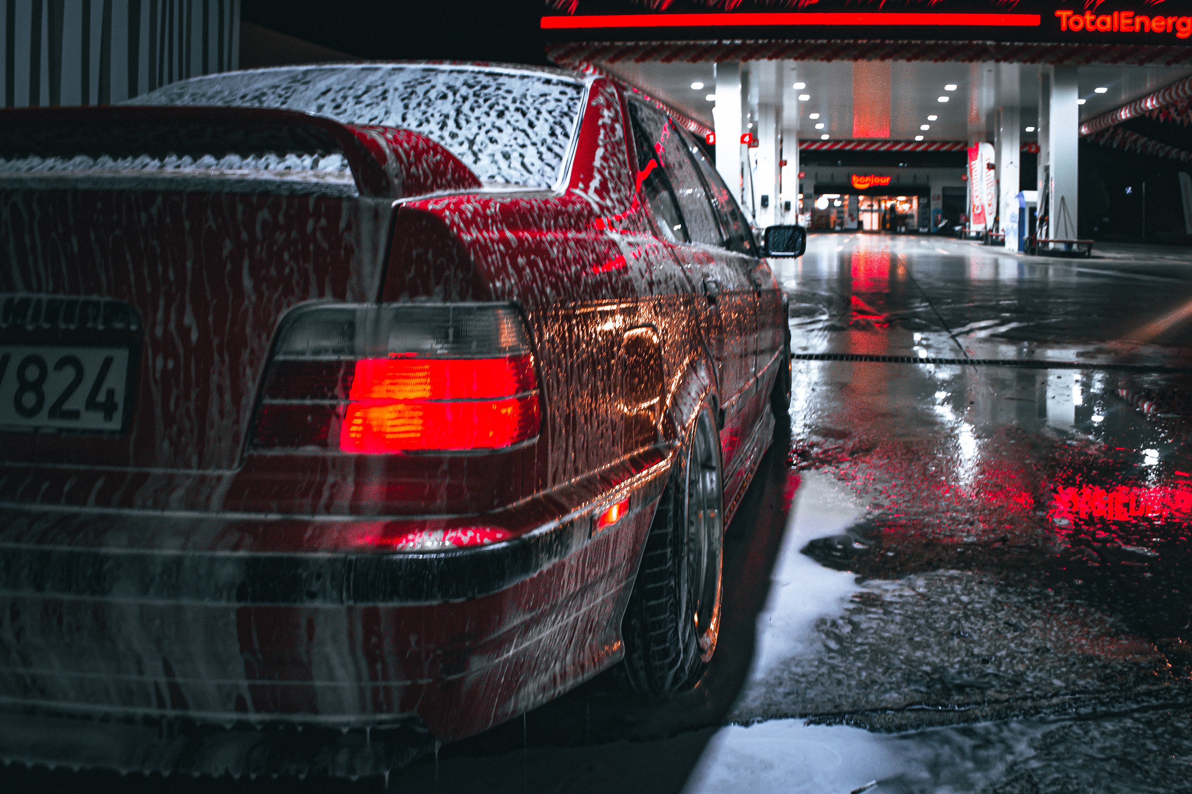 Red car being washed at night near a gas station