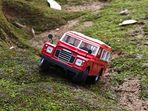 Free Close-up of a red diecast off-road vehicle navigating moss-covered terrain, showcasing miniature adventure. Stock Photo