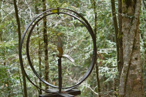 Free A metal bird sculpture encircled by hoops stands amidst the lush green forest. Stock Photo