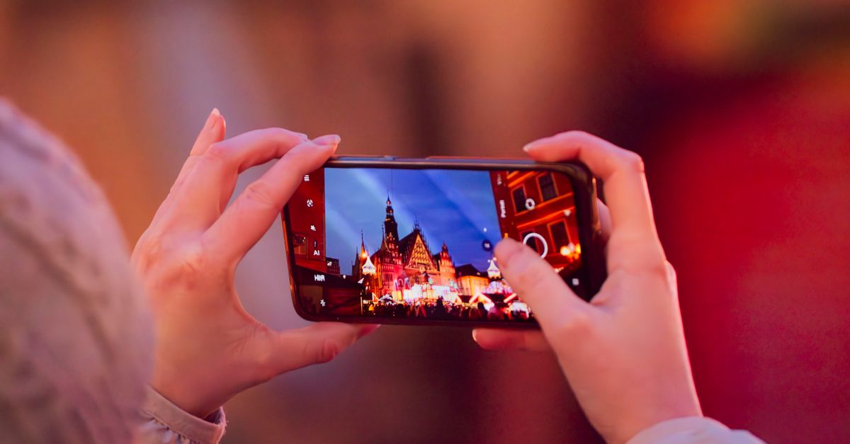 Um smartphone captura a colorida praça de mercado festiva de Wrocław com um vibrante brilho noturno.