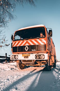 在冬天，一辆红色的卡车在晴朗的蓝天下沿着一条多雪的道路行驶