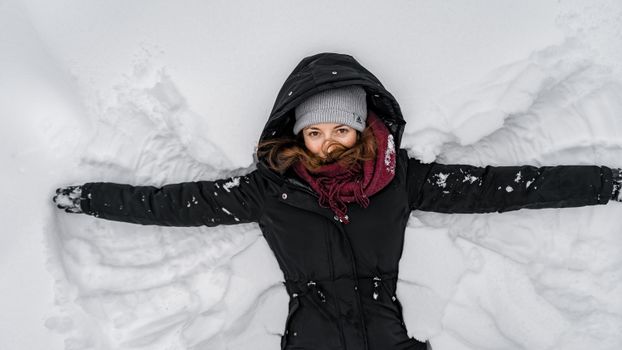 一名女子身着冬装，扮作雪地天使，在户外享受下雪的日子