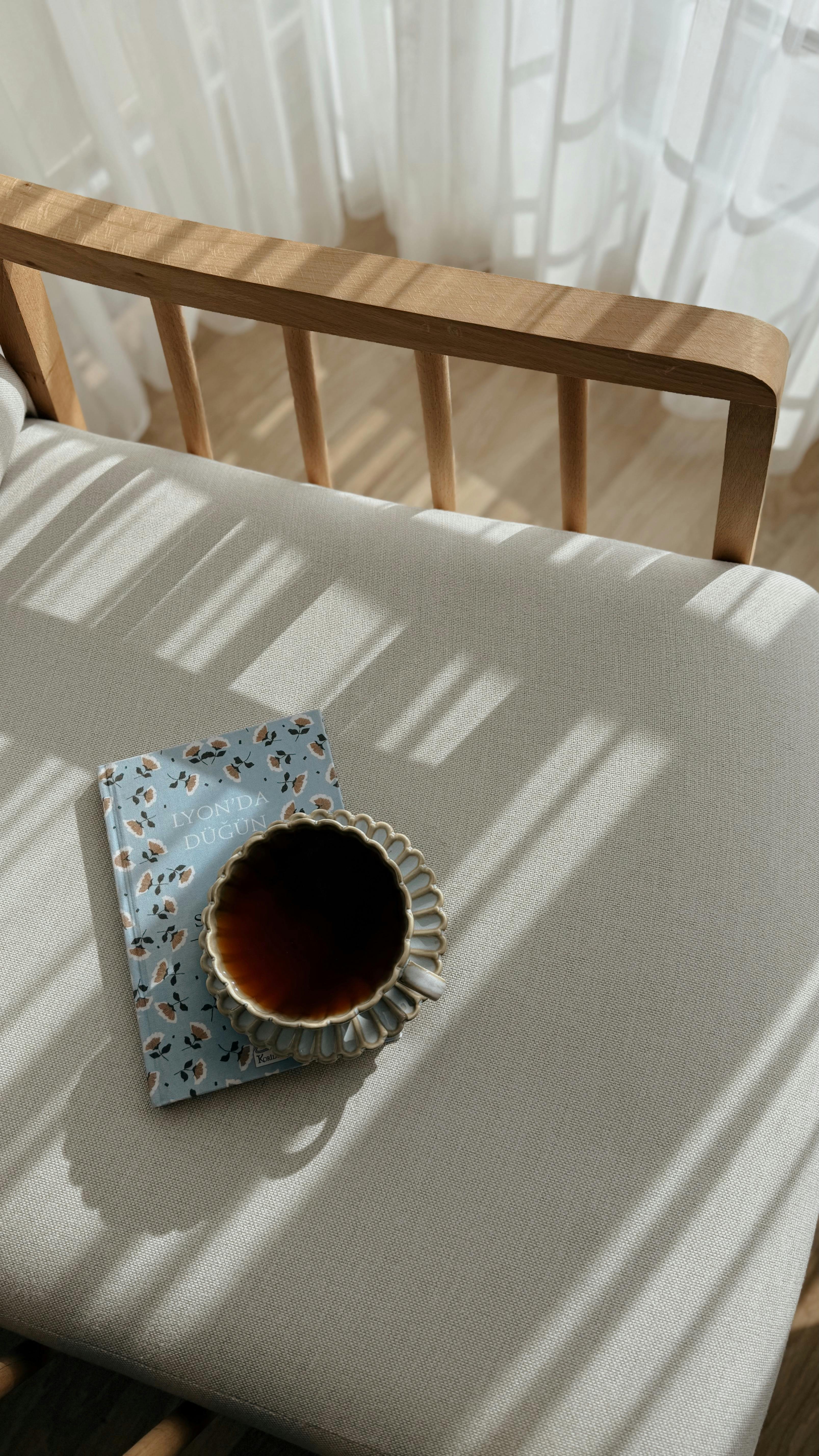 Gratis Una scena mattutina accogliente con una tazza di tè e un quaderno su una sedia di legno, immersi nella morbida luce del sole. Foto a disposizione