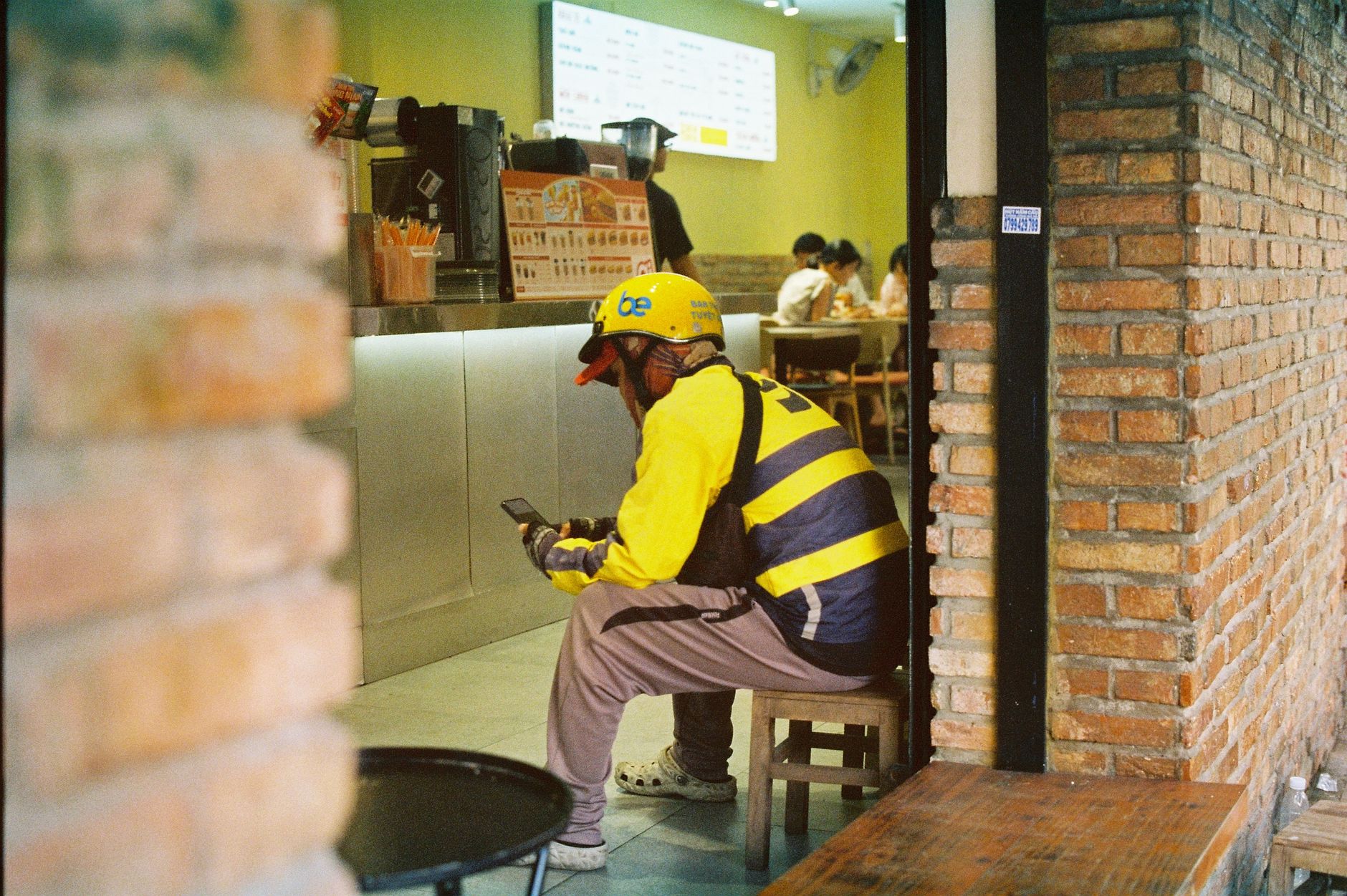 A delivery driver relaxes inside a Vietnamese cafe, engrossed in his smartphone.