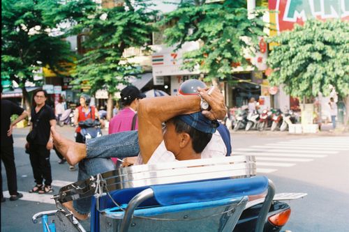Free Man relaxing on cyclo amidst bustling Ho Chi Minh City street. Stock Photo