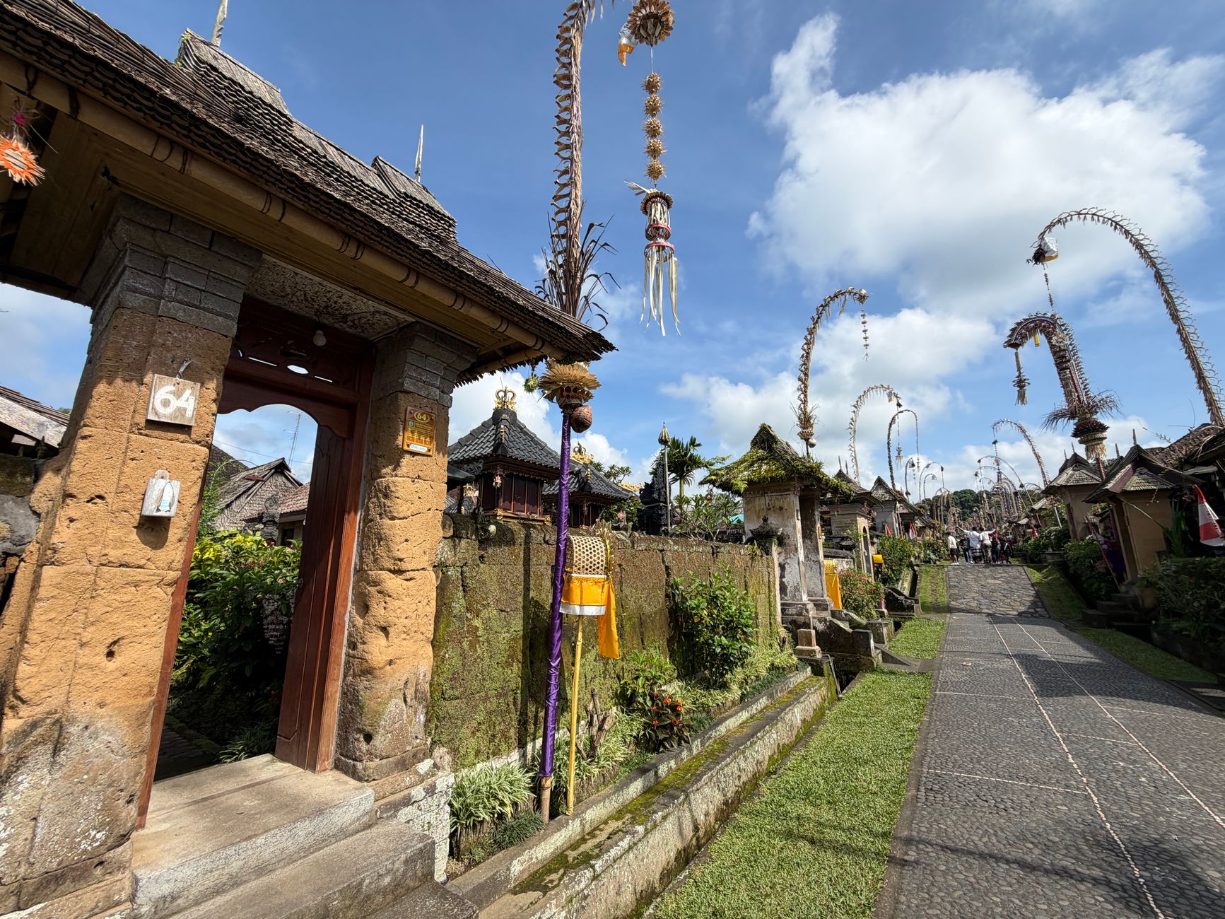 Traditional Balinese village courtyard prepared for a cockfight ritual, spectators gathered beneath temple decorations