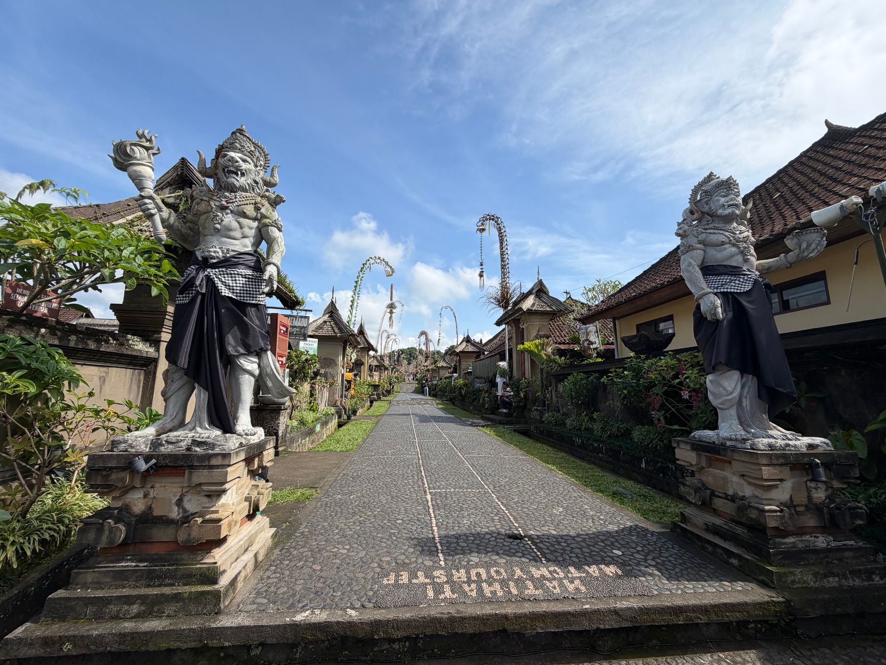 Peaceful Balinese street with stone guardian statues and traditional architecture.