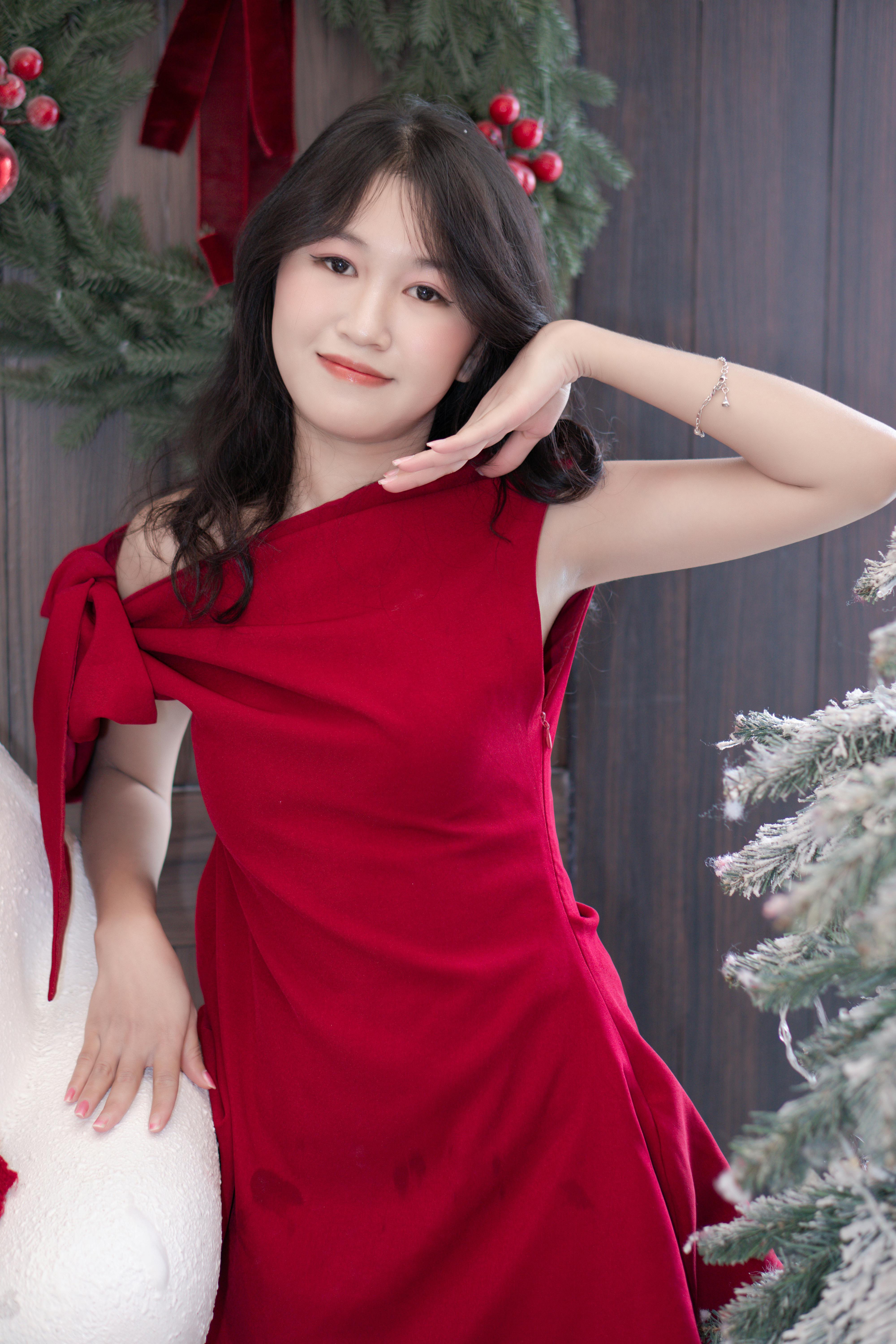 Woman in red dress posing amid Christmas decor and wreaths indoors.
