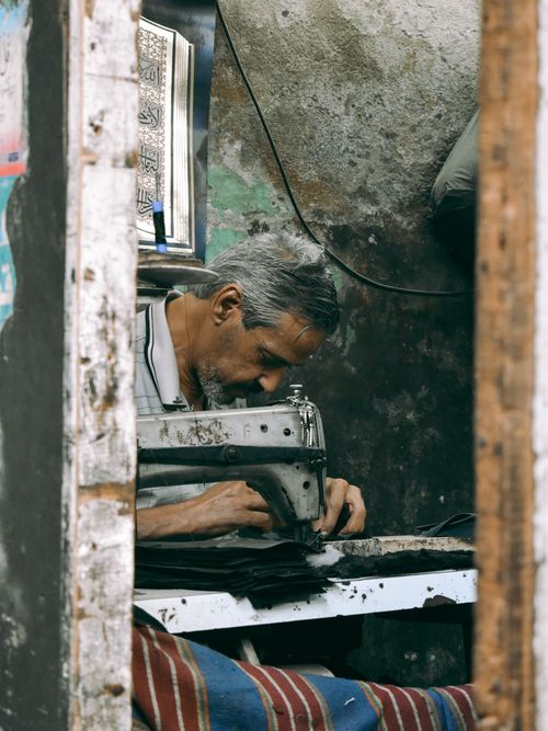 Free An elderly tailor intensely focused on sewing in a rustic workshop setting. Stock Photo
