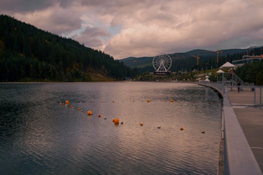 Tranquil lakeside view surrounded by mountains with a prominent Ferris wheel. Ideal for travel imagery.