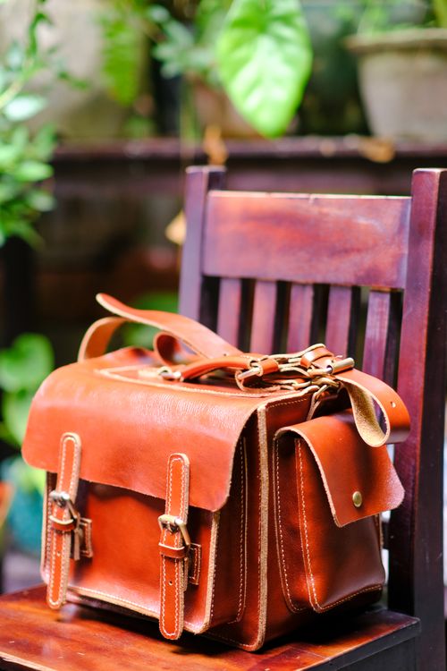Free Handcrafted leather bag displayed outdoors on a wooden chair in Hue, Vietnam. Stock Photo