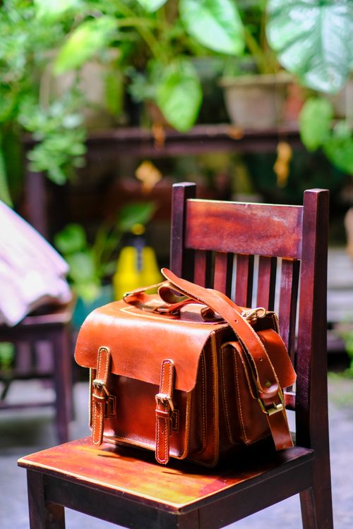 Free Handcrafted leather bag displayed on a wooden chair in a vibrant garden setting, showcasing Vietnamese artisanal craftsmanship. Stock Photo