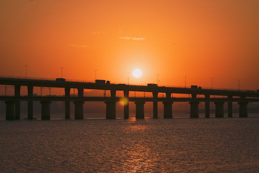 A stunning view of the sunrise over a bridge, casting a beautiful silhouette against the orange sky.