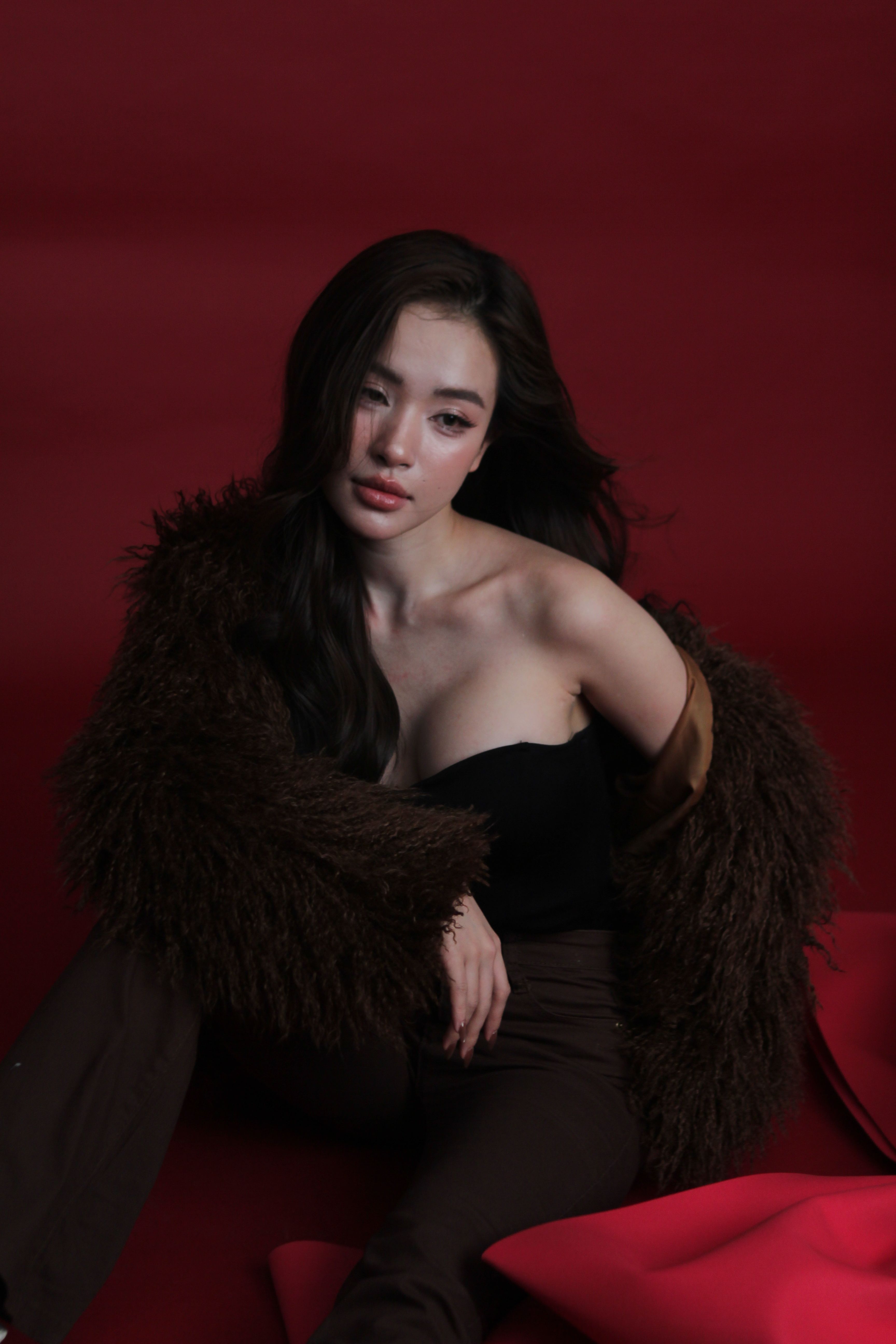 Stylish woman in a brown fur jacket posing gracefully against a red backdrop.