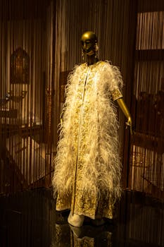 Golden mannequin showcasing elegant feathered gown in a dim-lit boutique setting.