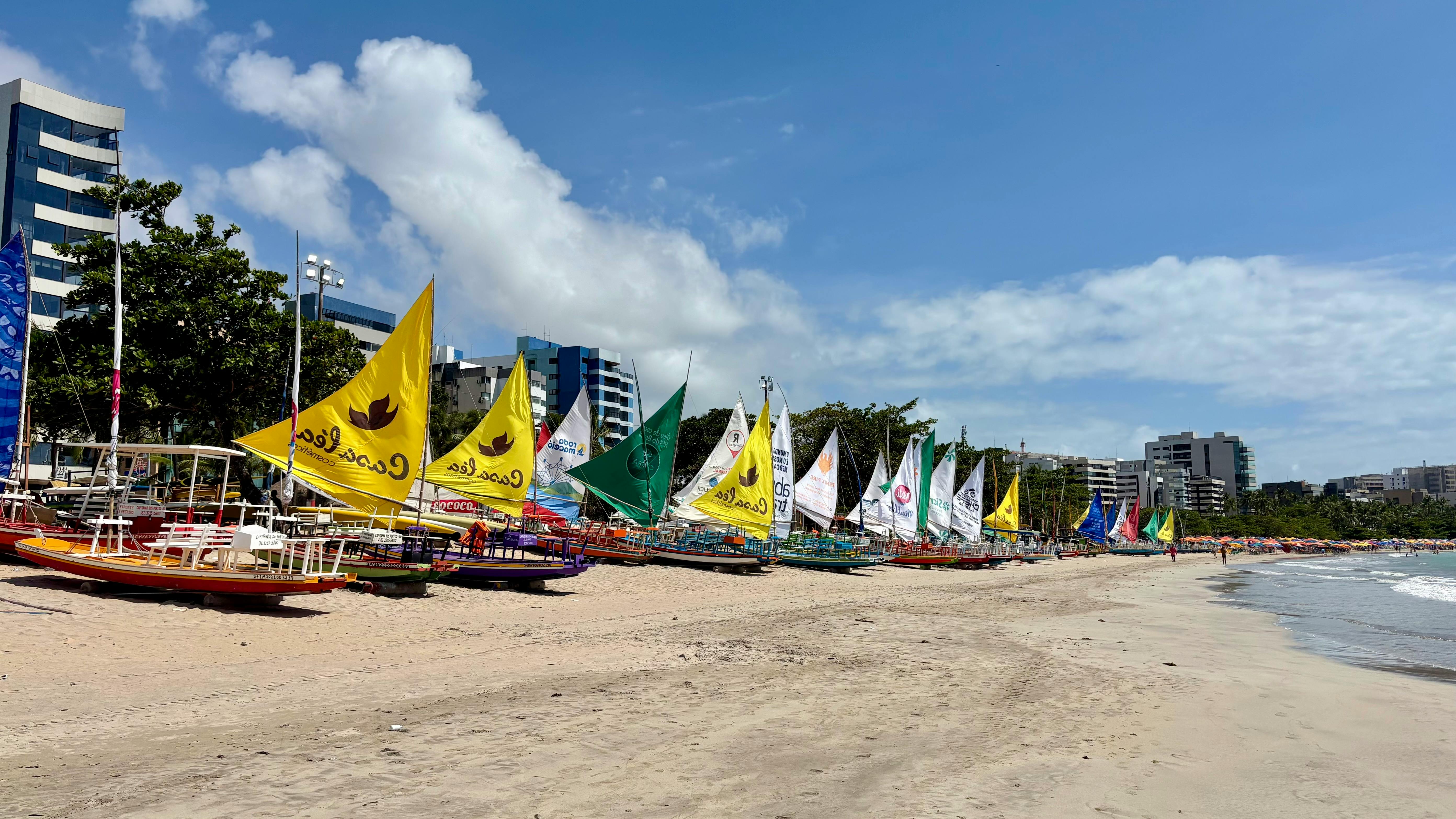 Vibrant sailboats lined up on Ponta Verde Beach in Maceió, Brazil, under a clear blue sky.