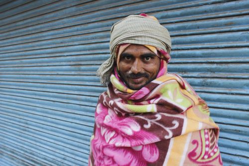 Free Man in traditional attire smiles warmly against a blue corrugated wall. Stock Photo