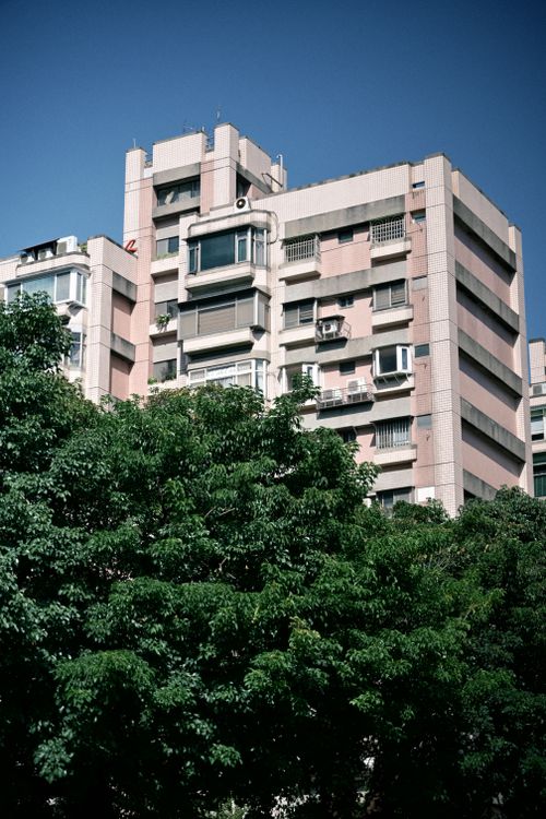 Free A pink high-rise building amidst lush green trees under clear blue skies. Stock Photo