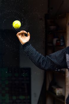 Fast spinning wet tennis ball thrown by crop man splashing water drops around