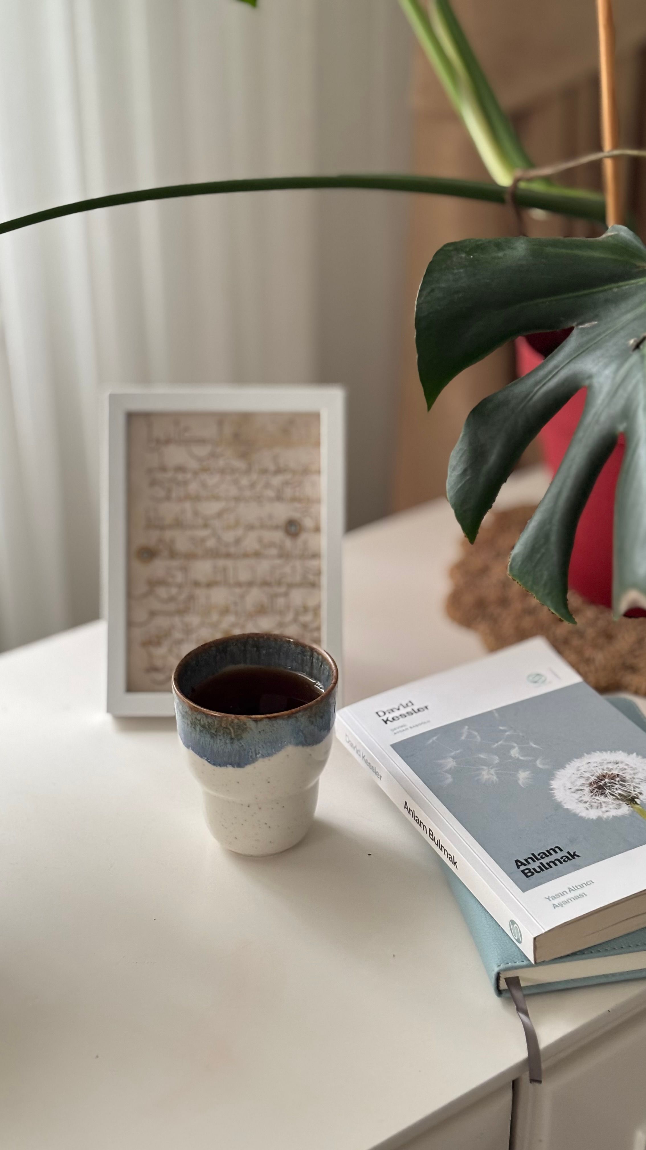 A cozy reading nook with a coffee cup, plant, and book on a white table.