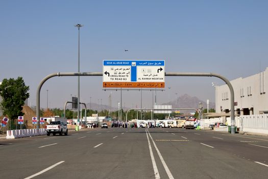 Road signage leading to Al Rahmah Mountain, Mecca, with vehicles and people on a sunny day.