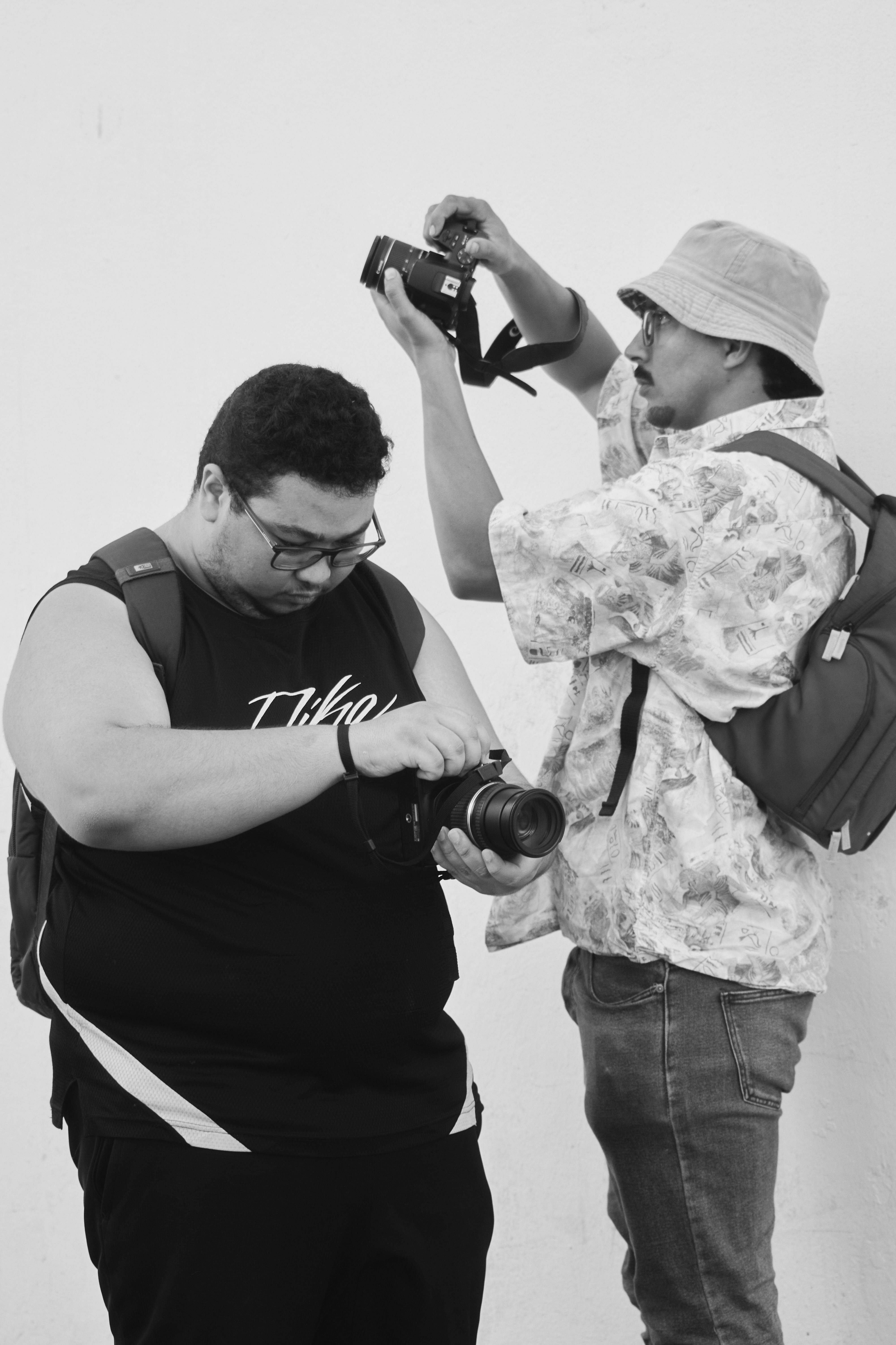 Two photographers equip themselves with cameras in a black and white capture.