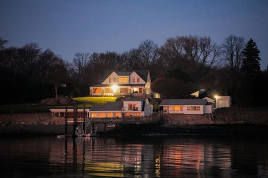 Charming lakeside house illuminated at dusk, reflecting on calm waters.