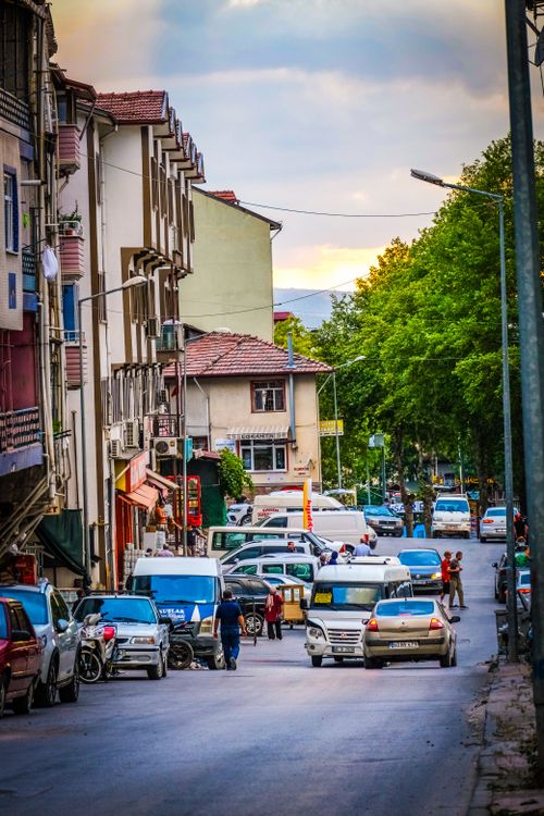 Free A bustling city street scene at dusk with cars and pedestrians under a colorful sky. Stock Photo