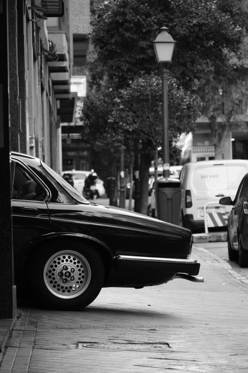 Free Black and white photo of a classic car parked on a city street, conveying a vintage urban atmosphere. Stock Photo